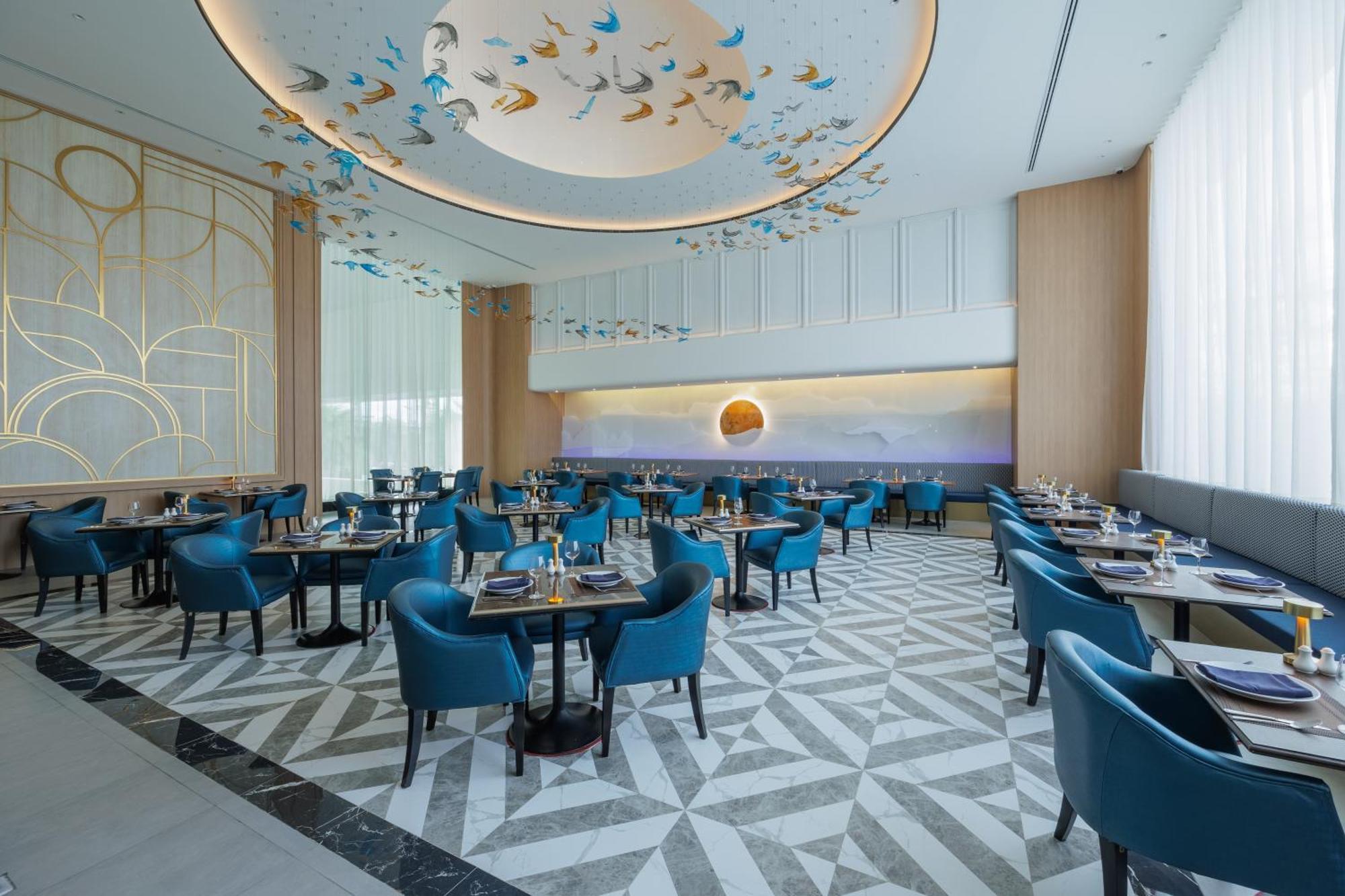 Siam Mandarina Hotel - Free Bkk Airport Shuttle Samut Prakan Exterior photo The photo depicts an elegant dining area of a restaurant. The space features a modern design with blue upholstered chairs around black tables. The flooring showcases a geometric pattern in light and dark shades, adding a stylish touch. The ceiling is