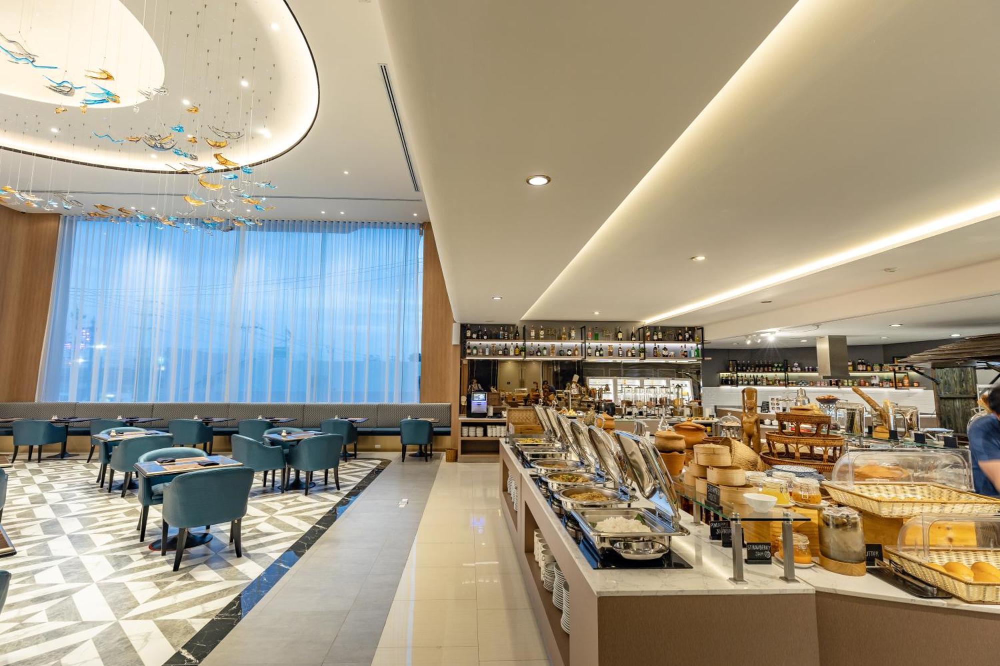 Siam Mandarina Hotel - Free Bkk Airport Shuttle Samut Prakan Exterior photo The photo depicts the interior of a modern restaurant or dining area. On the left side, there are several round tables with blue chairs arranged neatly. The flooring features a striking geometric pattern, adding to the aesthetic appeal. 

To the righ