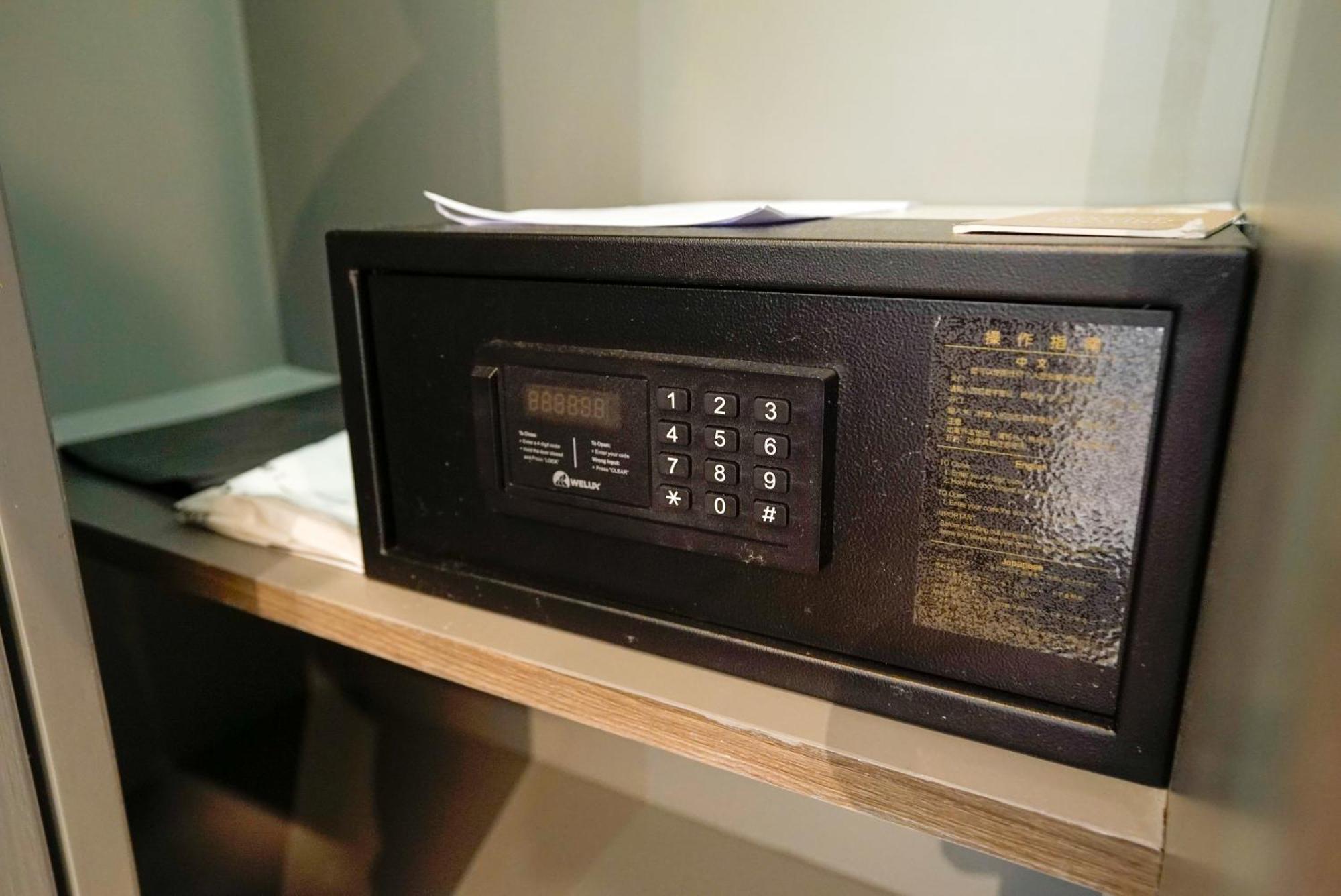 Siam Mandarina Hotel - Free Bkk Airport Shuttle Samut Prakan Exterior photo The photo shows a small, black electronic safe placed on a shelf. It features a keypad with numeric buttons, likely used for entering a security code to access the safe. Next to the safe, there are some sheets of paper, possibly documents or instruct