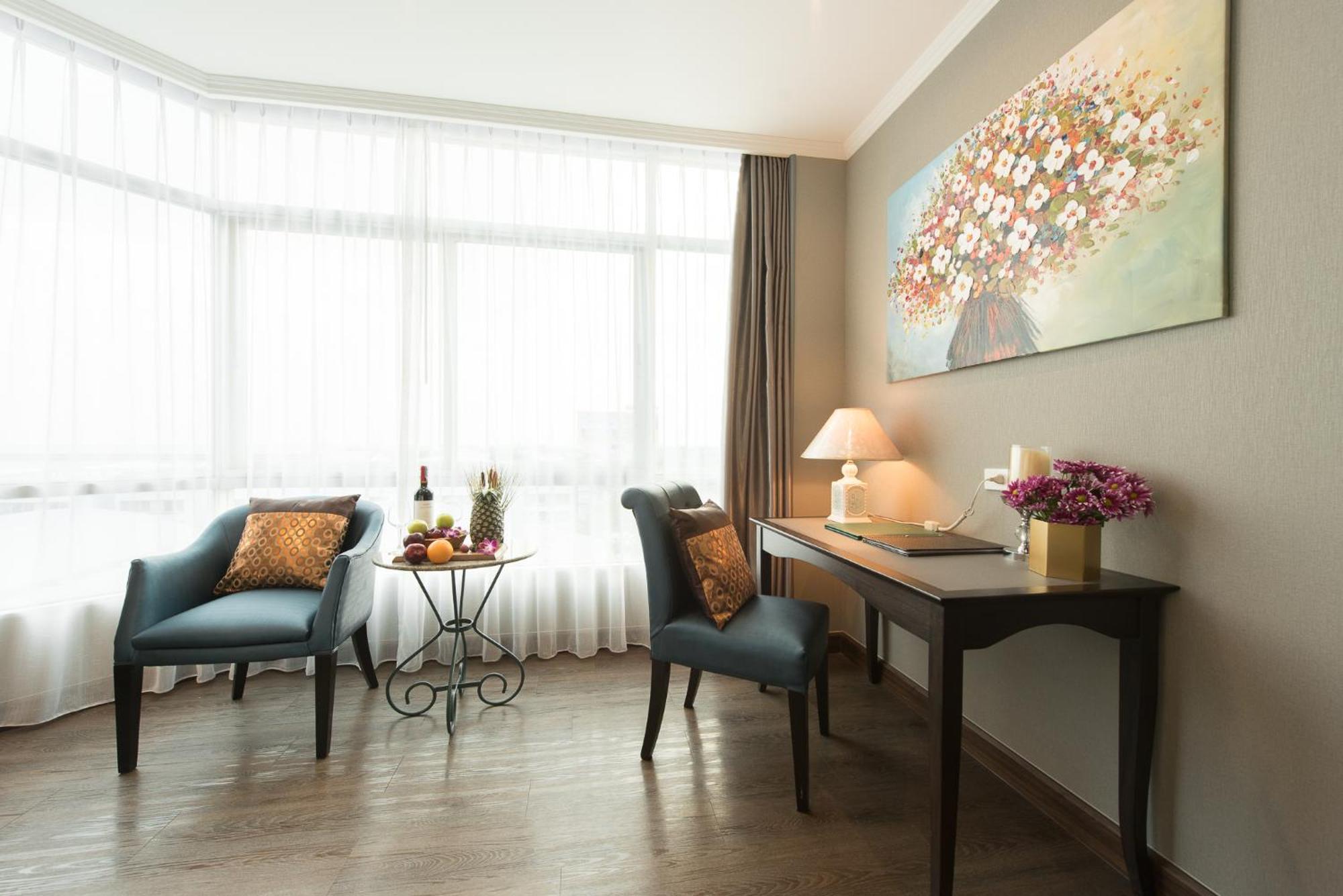 Siam Mandarina Hotel - Free Bkk Airport Shuttle Samut Prakan Exterior photo The photo shows a cozy interior of a room featuring a large window with sheer curtains that allow natural light to fill the space. On one side, there are two stylish blue armchairs, one with a decorative cushion, positioned near a small round table t