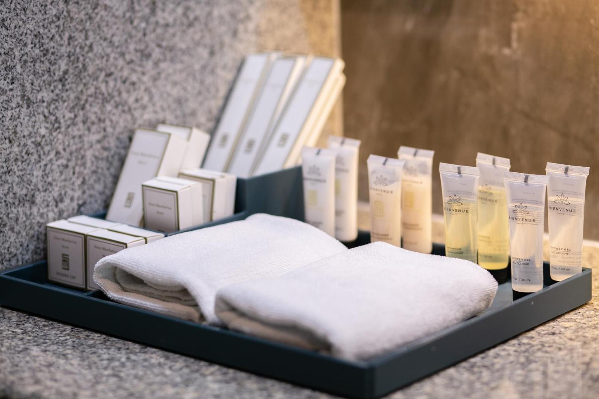 Siam Mandarina Hotel - Free Bkk Airport Shuttle Samut Prakan Exterior photo The photo shows a neatly arranged tray containing several items typically found in a hotel or spa setting. There are two white towels folded together, along with various toiletries. The toiletries include small bottles and tubes, likely containing sh