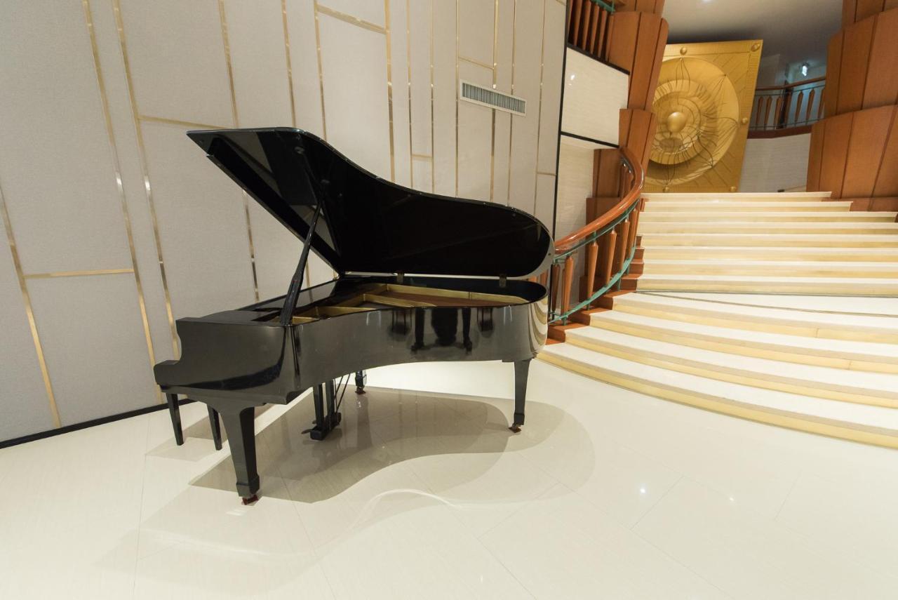 Siam Mandarina Hotel - Free Bkk Airport Shuttle Samut Prakan Exterior photo The photo shows a grand piano positioned in a well-lit interior space. The piano, which is black, is partially open, suggesting it is ready to be played. In the background, there is a stylish staircase leading up, and the walls feature elegant design