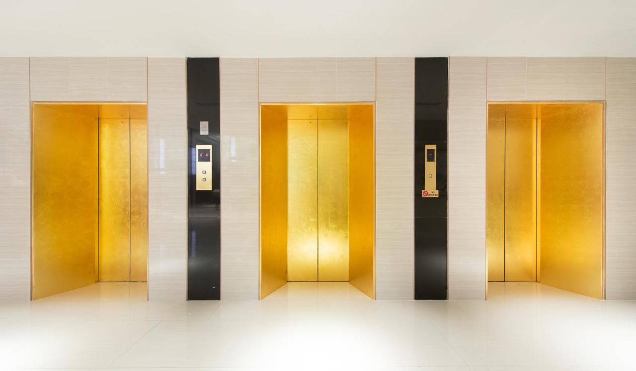 Siam Mandarina Hotel - Free Bkk Airport Shuttle Samut Prakan Exterior photo The photo shows a bank of elevators in a modern interior setting. There are four elevator doors, each with a sleek and shiny golden finish. The elevator doors are framed by black panels, creating a striking contrast with the gold. On the left side of